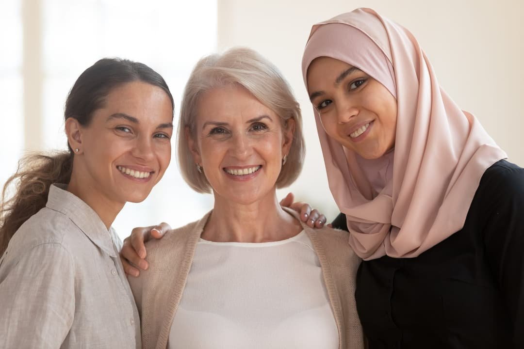 Three women of different generations standing close together and smiling.